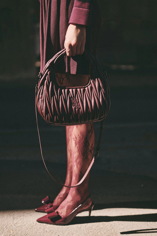 Bolso acolchado burdeos con bandolera, llevado en la mano